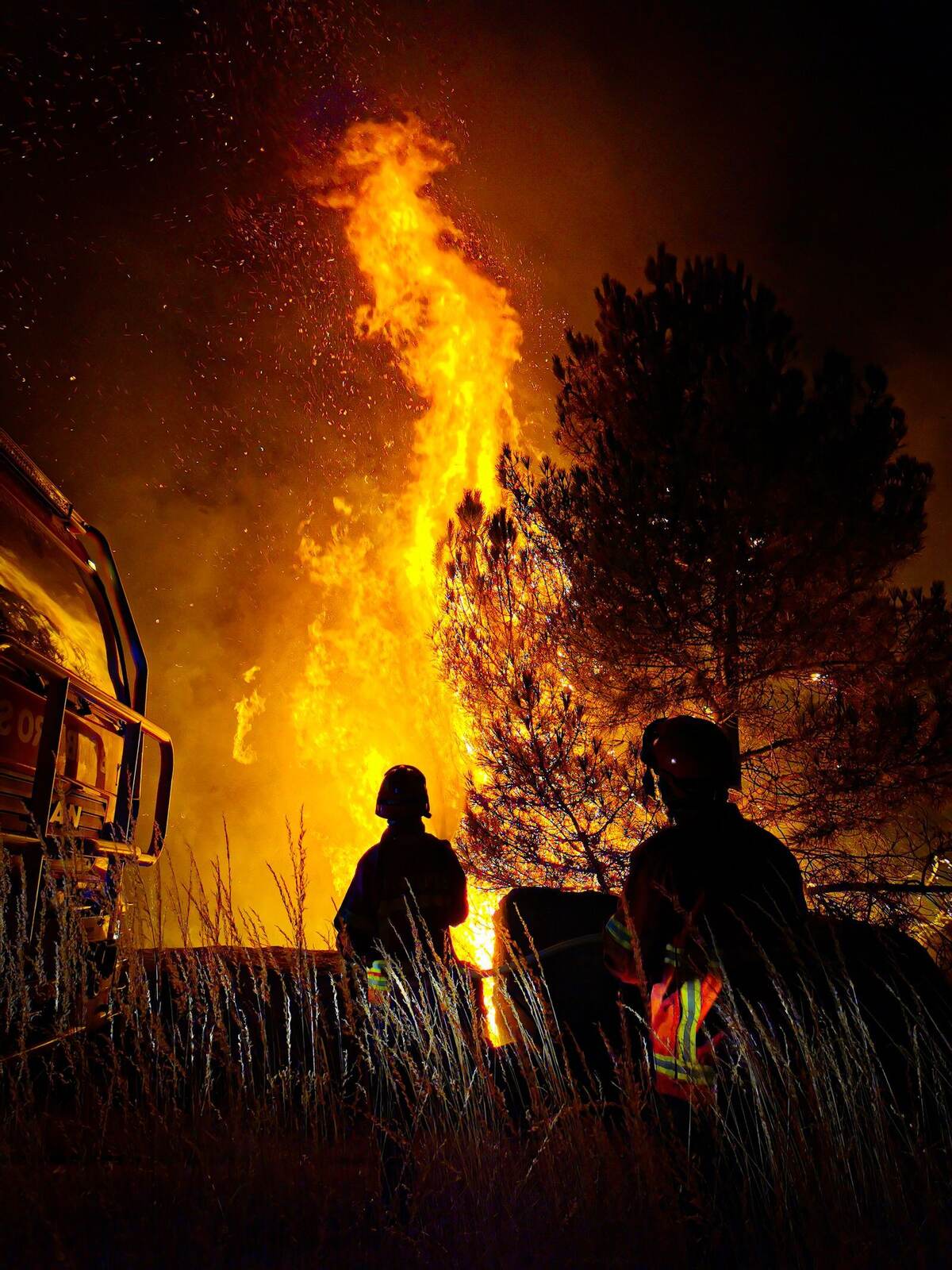 Firefighters silhouetted against a wildfire at night.