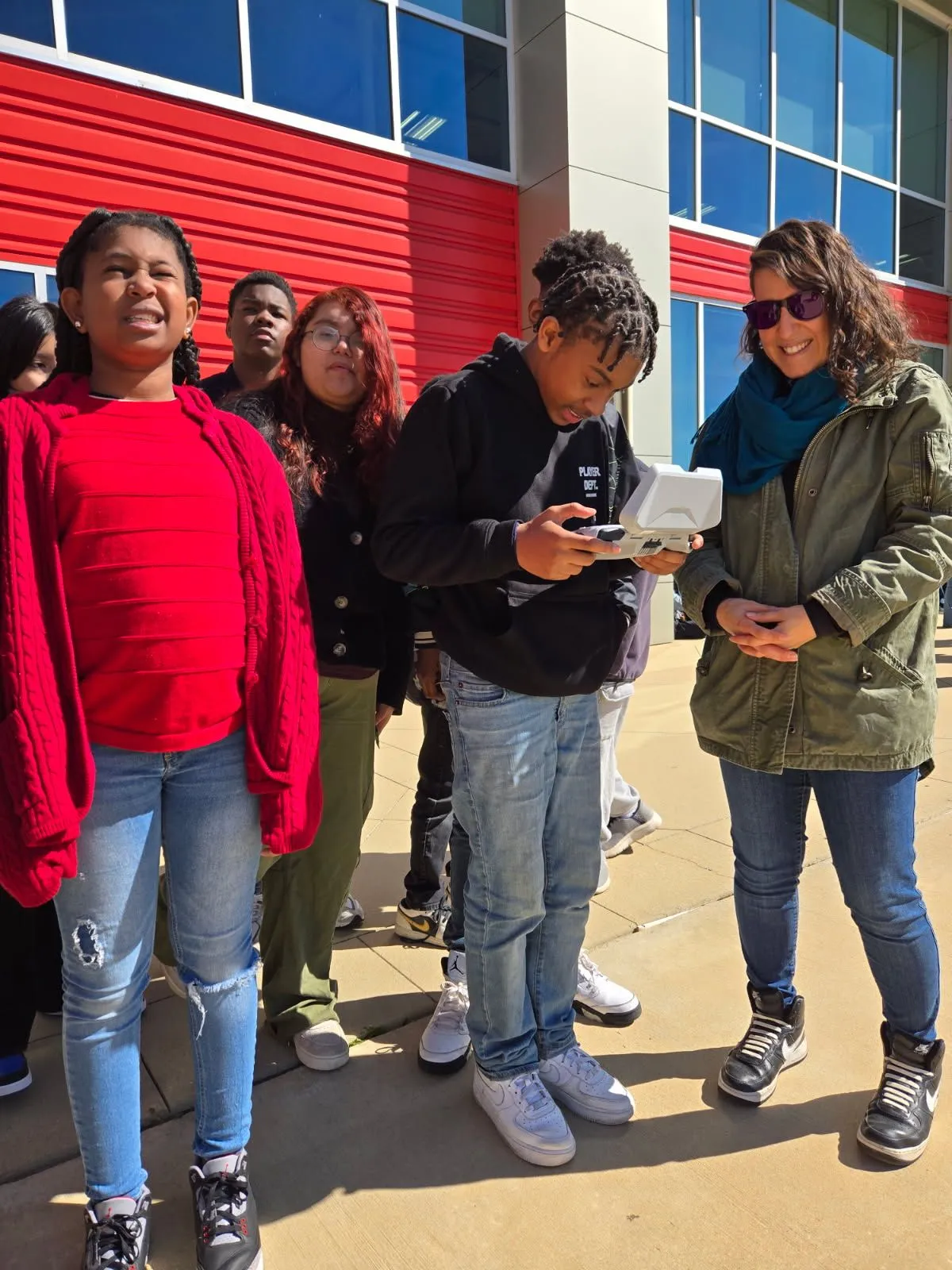 A student holding a drone controller outside a Philadelphia school, with an adult beside him