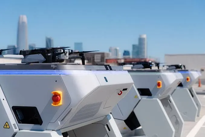 Row of white drone docks on a rooftop with a city skyline
