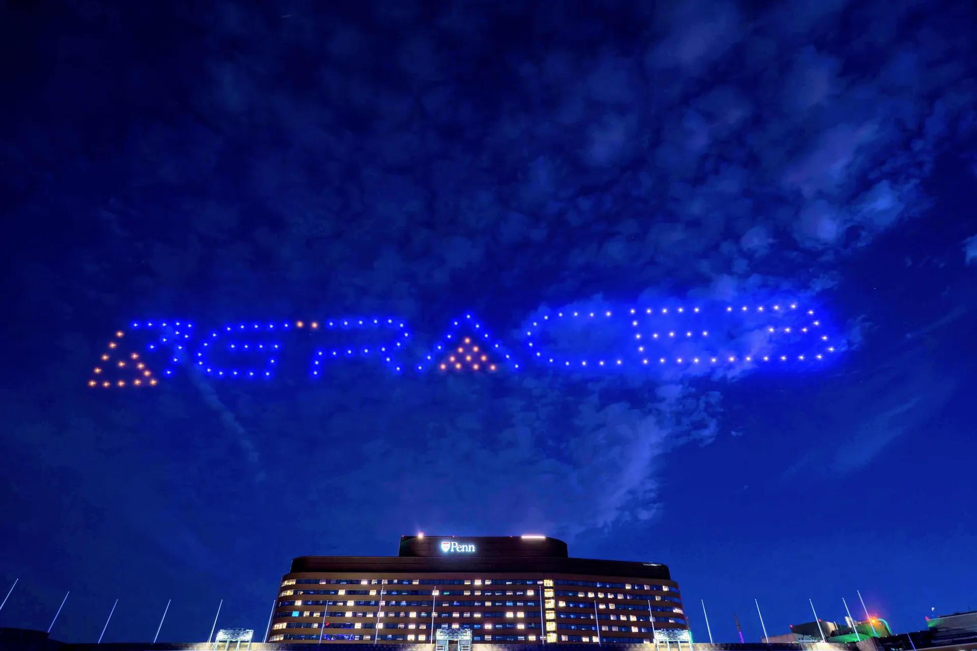 Blue drone lights spelling Happy 30th Birthday above a Penn campus building at night