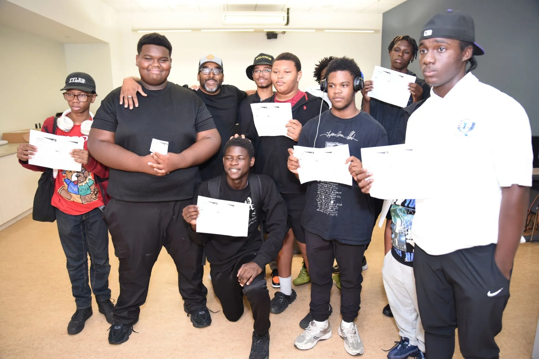 A mentor and a large group of students holding certificates together in a classroom