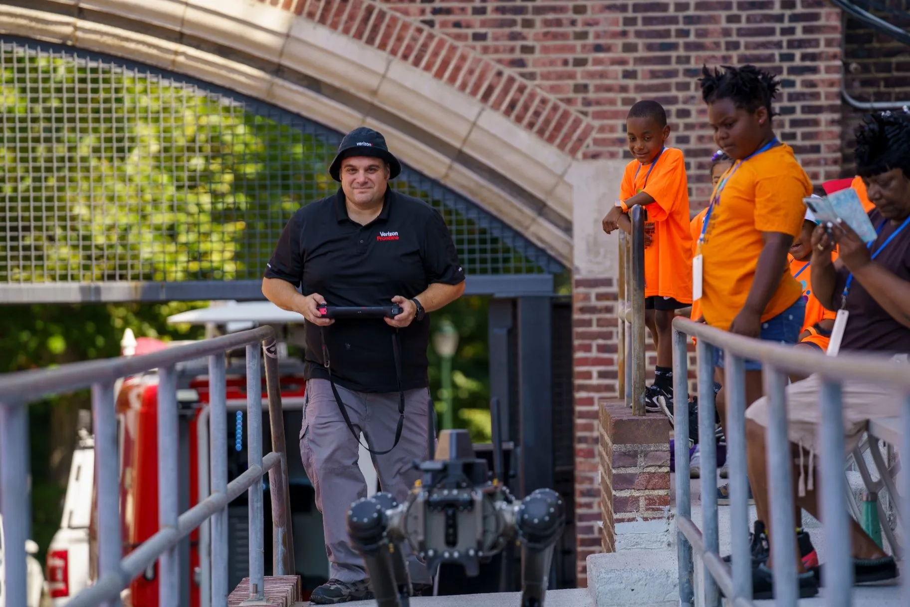 A mentor operating a four-legged robot while students watch from the steps